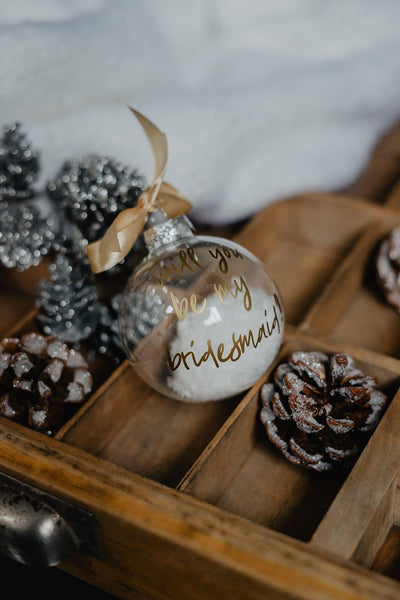 Christbaumkugel aus transparentem Glas mit goldener Schrift "will you be my bridesmaid" und goldener Schleife und Schneebefüllung aus Plastikschnee